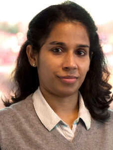 Frau Singha mit dunklem Haar und hellblauer Bluse, ernster Ausdruck.